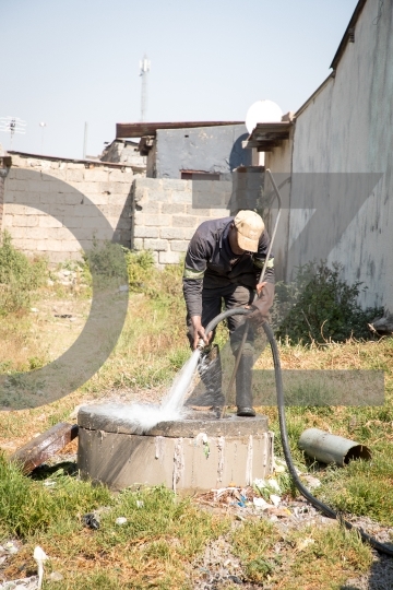 Worker cleaning manhole using hose and water